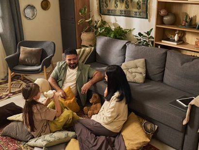 Family enjoying quality time together in cozy living room with carpeted floor and modern furniture, playing with plush toys and using electronic device, having fun and bonding